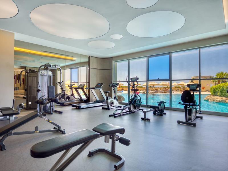 Palestra moderna con attrezzi e vista sulla piscina esterna.