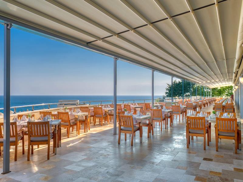 Terrazza aperta con sedie e tavoli in legno con vista sul mare sotto un cielo limpido.