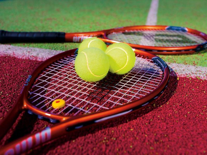 Due palline da tennis sono posate su una racchetta su un campo rosso e verde.
