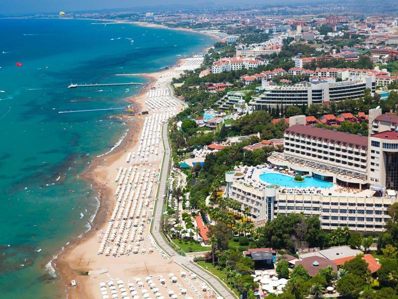 Vista aerea di un hotel vicino a una lunga spiaggia sabbiosa con ombrelloni e mare blu.