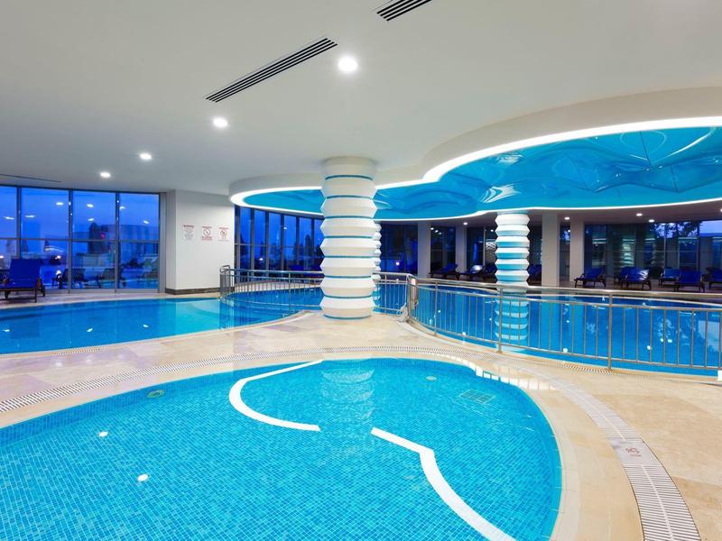 Piscina coperta luminosa con illuminazione moderna e vista sul tramonto attraverso grandi finestre.