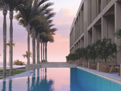 Piscine moderne d'hôtel avec palmiers et vue sur la mer au coucher du soleil.