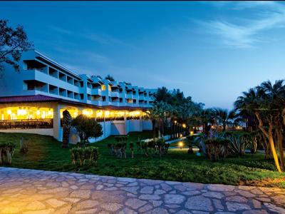 Complexe hôtelier éclairé avec terrasse, piscine et jardin soigné au crépuscule