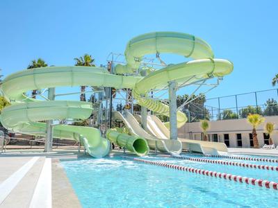 Grande toboggan aquatique verte menant à une piscine extérieure sous un ciel dégagé.