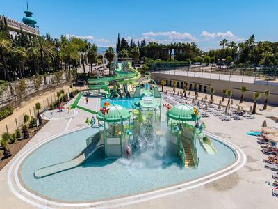 Parc aquatique avec toboggans, jeux d'eau et chaises longues par une journée ensoleillée.