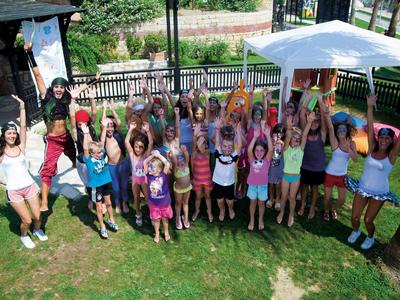 Groupe d'enfants et deux adultes debout dans un jardin devant un pavillon, les mains levées.