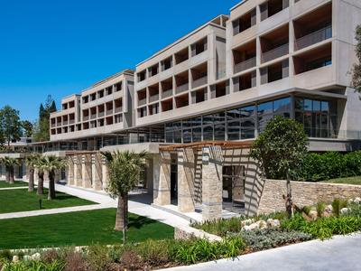 Hotel moderno con più piani, grandi balconi e giardino curato sotto il sole.