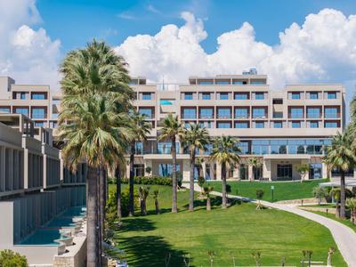 Complesso alberghiero moderno con palme e aree verdi ben curate sotto un cielo azzurro con nuvole.