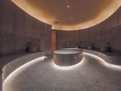Bagno turco circolare con illuminazione indiretta e pareti in pietra scura.
