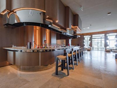 Area bar moderna dell'hotel con bancone elegante e sgabelli alti in ambiente luminoso.