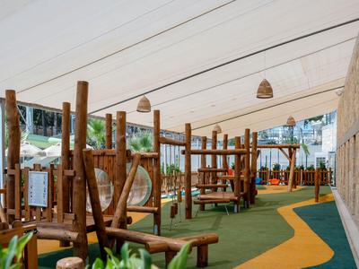 Parco giochi coperto per bambini con strutture in legno e pavimentazione verde in ambiente alberghiero
