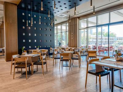 Ristorante moderno con mobili in legno e grandi finestre che permettono l'ingresso della luce naturale.