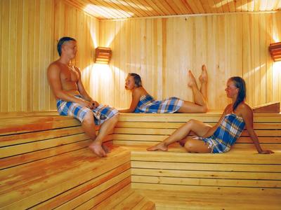 Trois personnes se détendent dans un sauna en bois avec des serviettes.