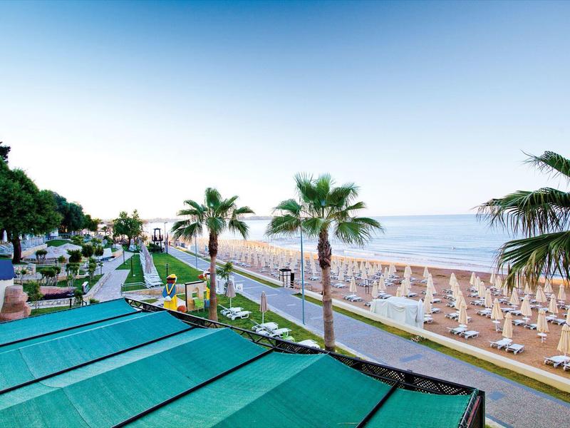 Vue d'une plage avec parasols, palmiers et une promenade en bord de mer.