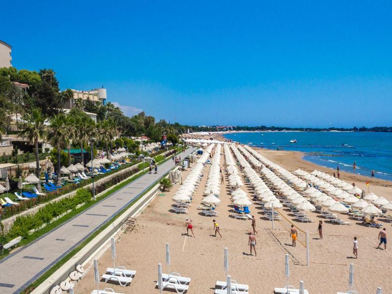 Large plage de sable avec rangées de parasols et transats près de la promenade et de la mer.