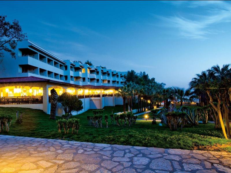 Complexe hôtelier éclairé avec terrasse, piscine et jardin soigné au crépuscule