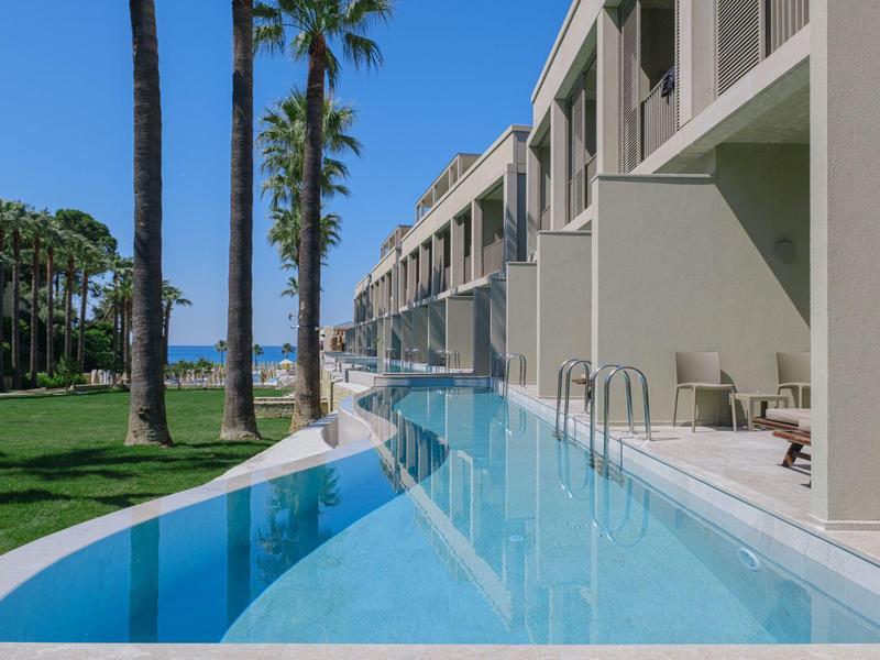 Hôtel avec longue piscine extérieure, palmiers et pelouse verte à côté du bâtiment.