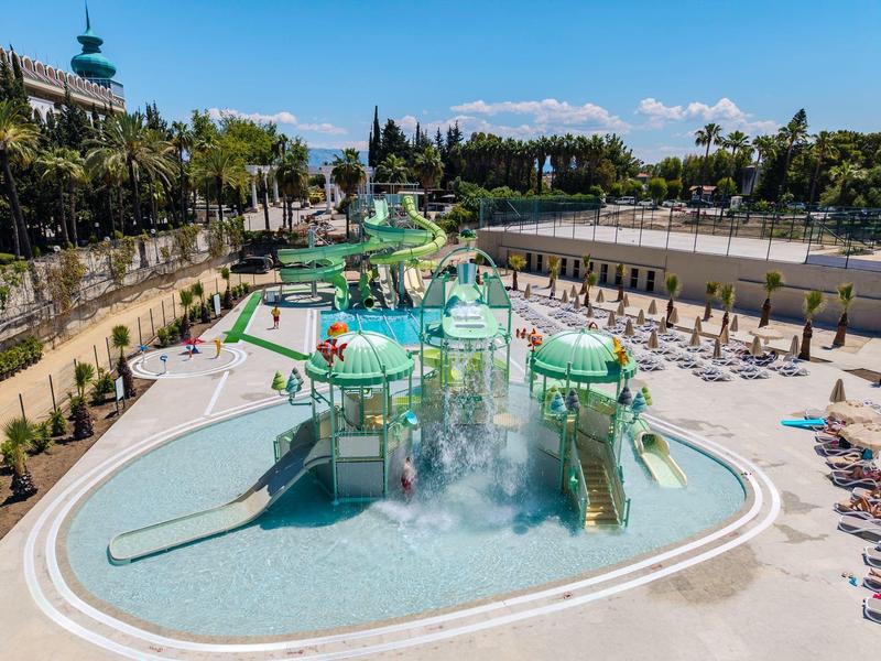 Parc aquatique avec toboggans, jeux d'eau et chaises longues par une journée ensoleillée.