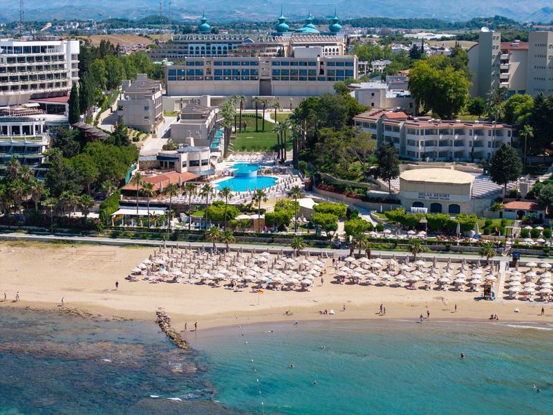 Complexe hôtelier avec piscine, chaises longues sur la plage et mer turquoise.
