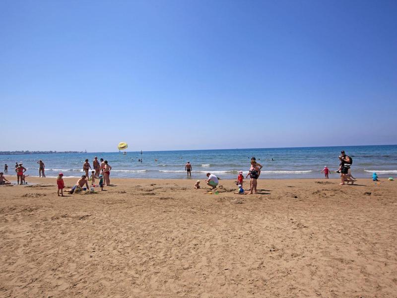 Plage avec du sable, des gens jouant près de l'eau et un ciel bleu clair.