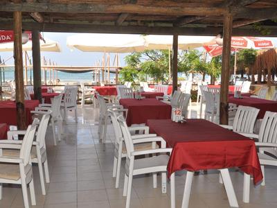 Offenes Restaurant am Meer mit weißen Stühlen und Tischen, die rot gedeckt sind.