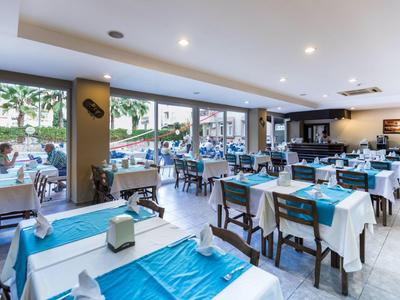 Helles, modernes Restaurant mit Holztischen, weißen Decken und blauen Tischdeckern, große Fenster.