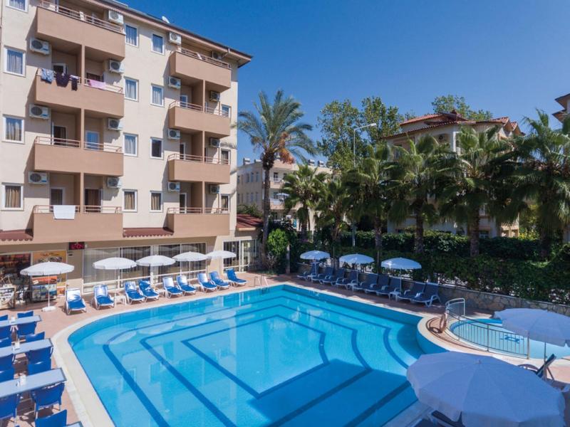 Piscina moderna de hotel con tumbonas y sombrillas rodeada de palmeras y edificios.