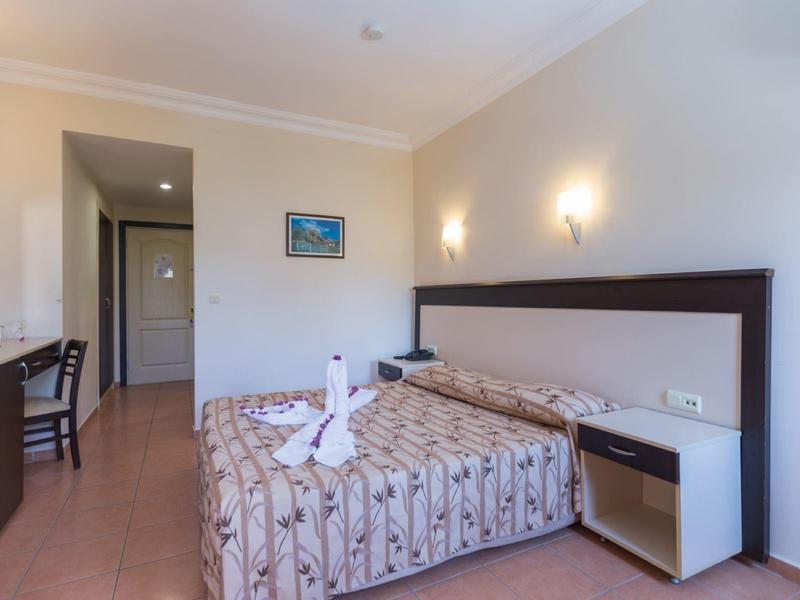 Habitación de hotel luminosa con cama doble, escritorio, silla y un cuadro en la pared.