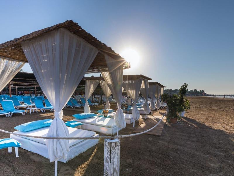 Playa con sombrillas, cortinas blancas y tumbonas azules al atardecer.