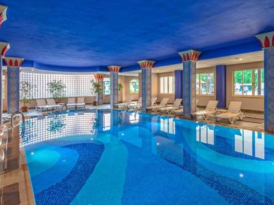 Basen kryty z dekoracyjnymi kolumnami i leżakami przy oknach.