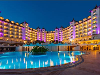 Oświetlony hotel z dużym, okrągłym basenem pod nocnym niebem.