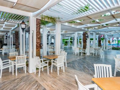 Ristorante all'aperto con tavoli e sedie bianchi sotto una terrazza coperta.