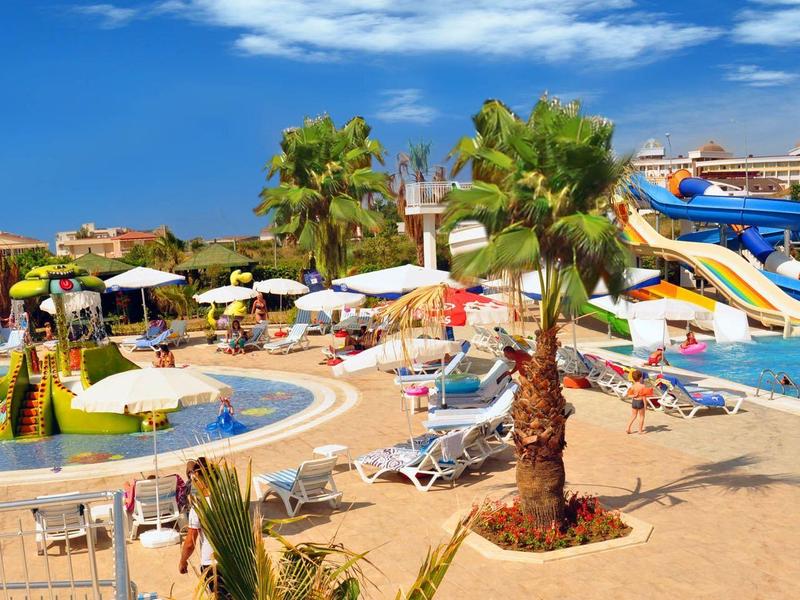 Tętniący życiem basen w ośrodku z zjeżdżalniami wodnymi i palmami pod niebieskim niebem.