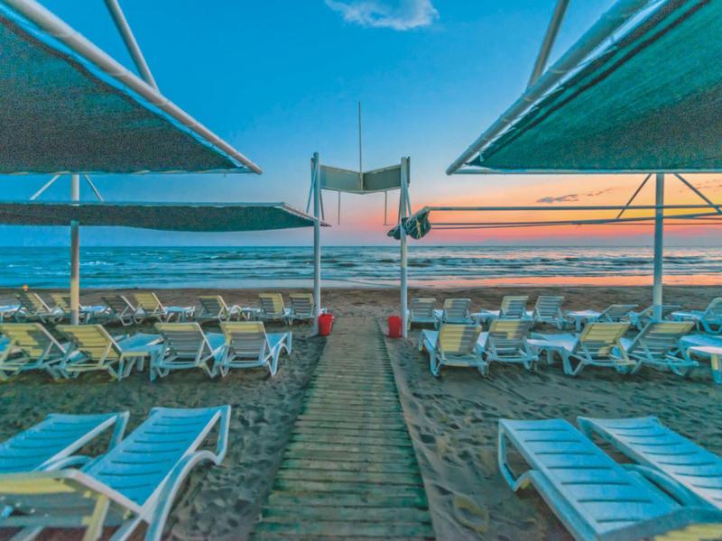 Plaża o zachodzie słońca z leżakami i parasolami w rzędach.