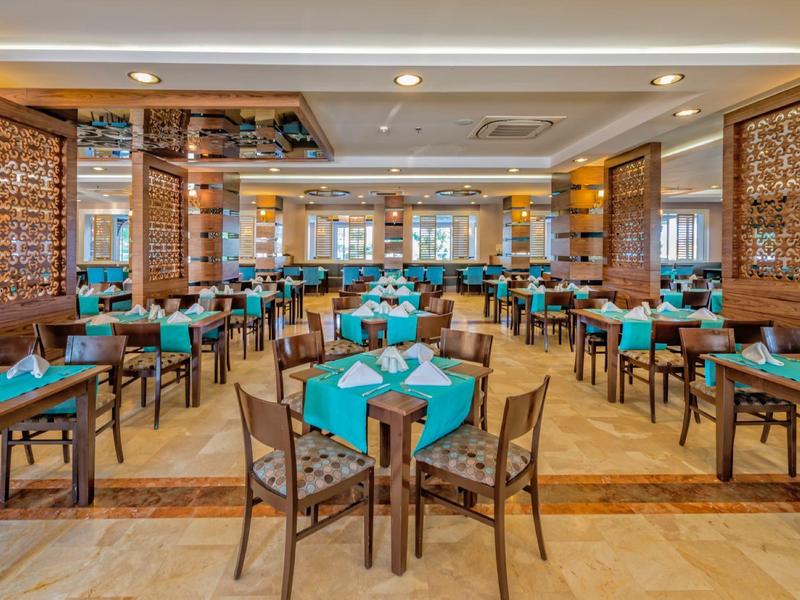 Przestronna jadalnia z drewnianymi stołami i turkusowymi serwetkami.