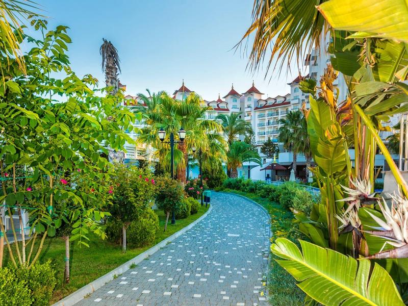 Wybrukowana ścieżka między bujną roślinnością prowadząca do hotelu pod jasnym niebem.