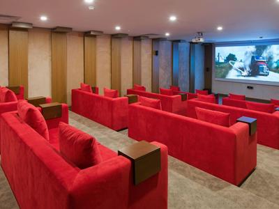 Pequeña sala de cine con sofás rojos y pantalla grande para películas.