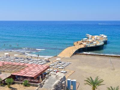 Playa con sombrillas, tumbonas y un largo muelle que se adentra en el mar azul.