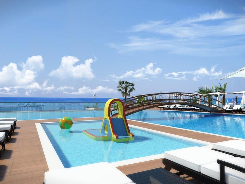 Piscina moderna de hotel con sombrillas, tumbonas y vista al océano bajo un cielo azul.