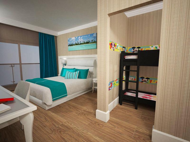 Habitación de hotel con cama doble, escritorio, litera colorida en habitación contigua y suelo de madera.