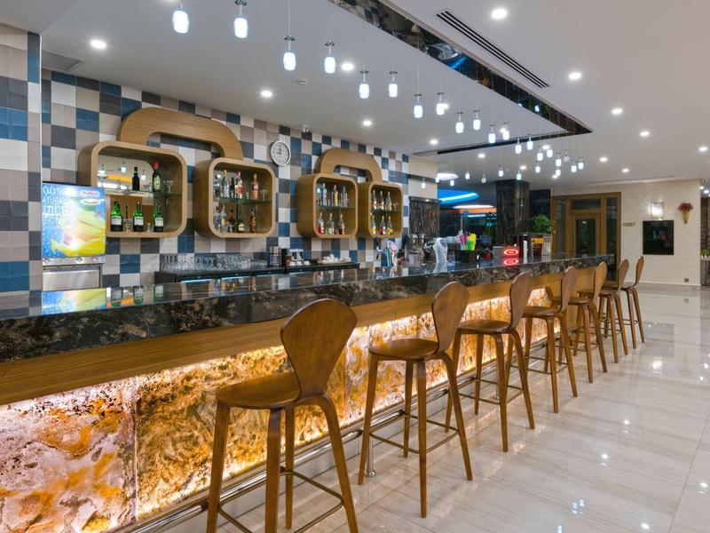 Área moderna de bar de hotel con mostrador de piedra iluminado y taburetes de madera sobre suelo brillante.