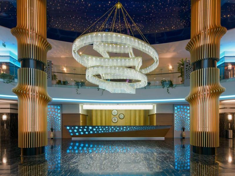 Lobby de hotel lujosa con gran candelabro, suelo brillante y recepción moderna.