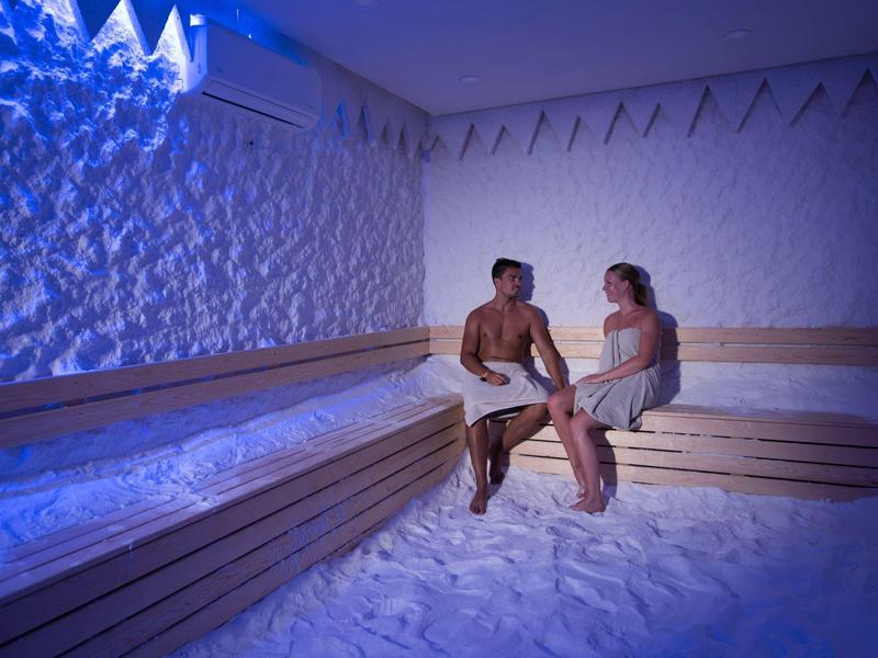 Un hombre y una mujer se relajan en una sala de inhalación de sal iluminada en azul con suelo de arena.