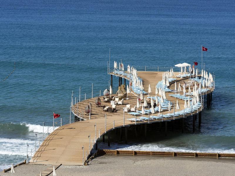Muelle curvo con sombrillas y sillas junto al mar y olas suaves en la playa.