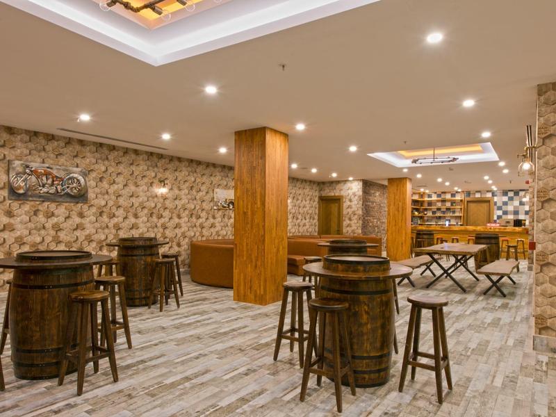 Vista interior de un bar elegante en un hotel con barra de madera y taburetes sobre suelo claro con patrón.