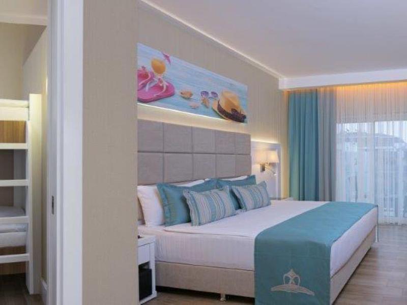 Habitación de hotel moderna con cama doble, litera, escritorio y balcón con vista al mar.