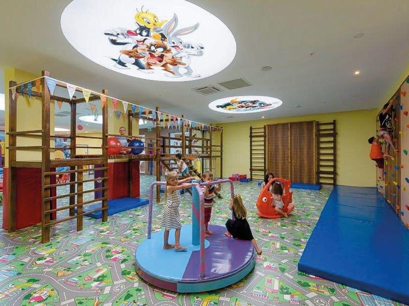 Área de juegos infantil interior colorida con estructuras para escalar y colchonetas en un hotel.