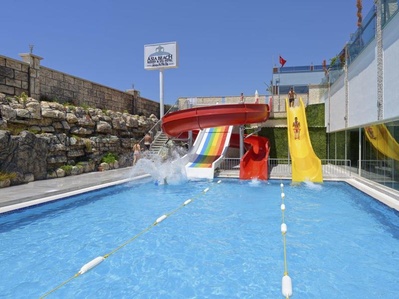 Piscina vacía con dos toboganes de colores junto a un muro de piedra bajo un cielo azul.