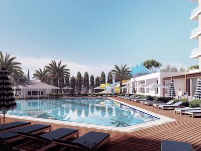 Moderne zwembadomgeving met ligstoelen, parasols en palmbomen naast een hotelgebouw.