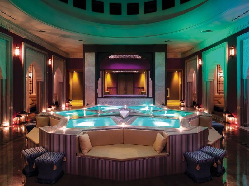 Vista interior de una lujosa zona de spa con jacuzzi central y luz tenue.